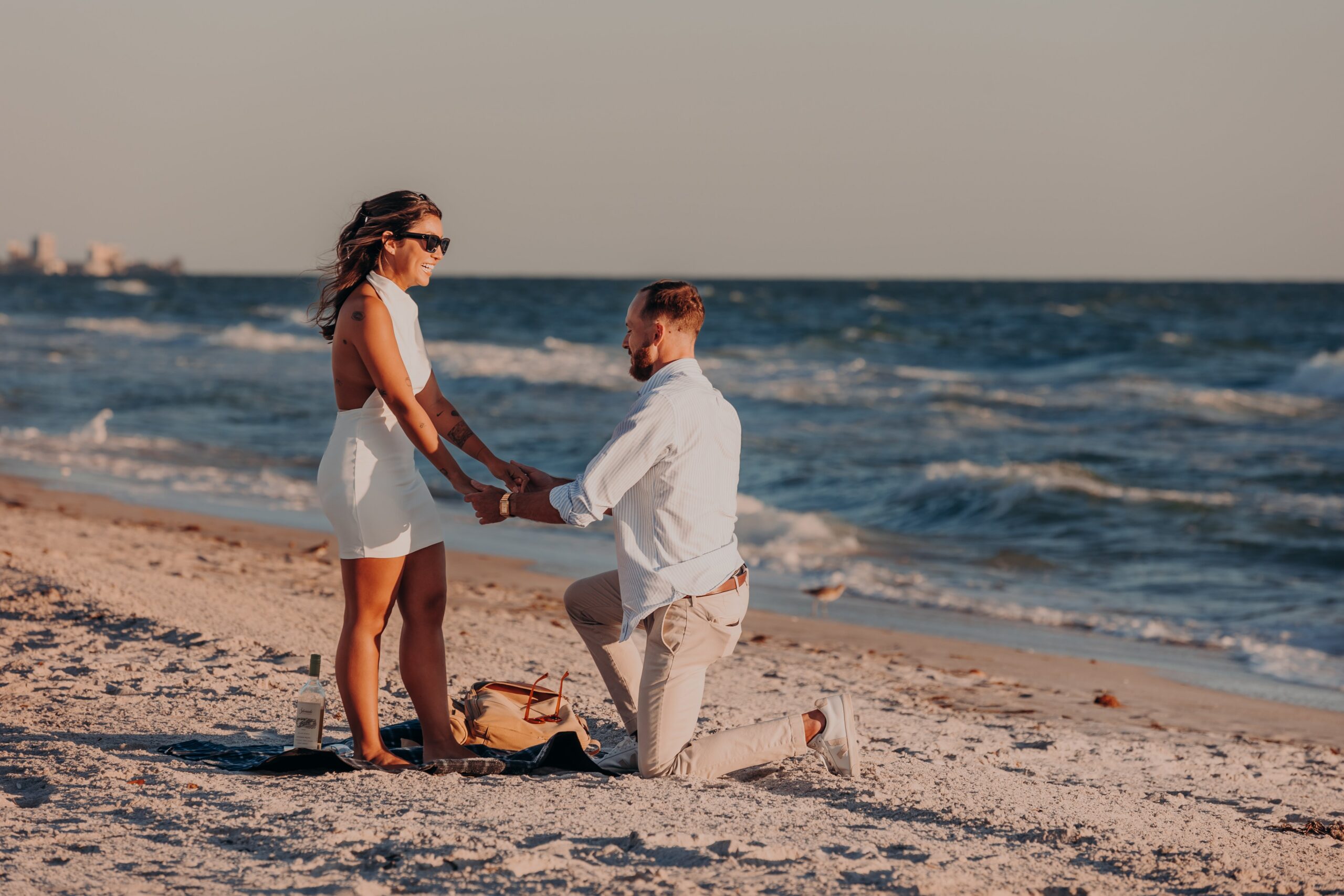 Sarasota beach proposal — Patrick proposing to Bianca on one knee at the Gulf of Mexico shoreline, photographed by Angela Moon Photography