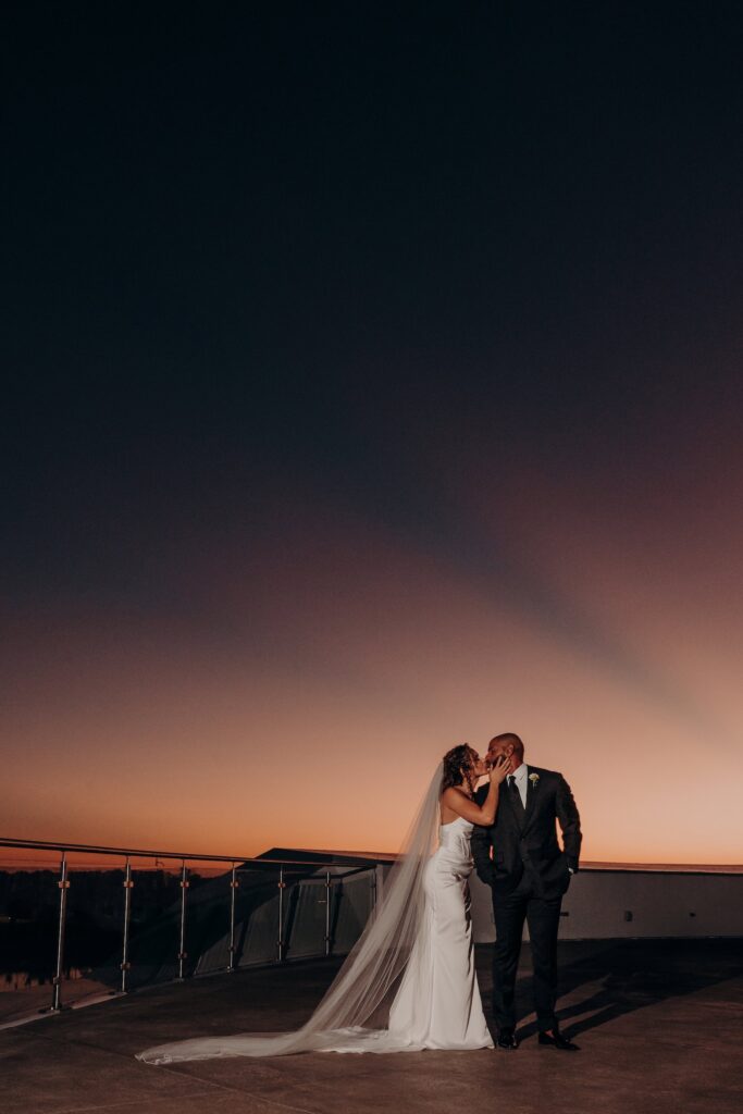 Bride and groom kissing at sunset on the rooftop terrace at Mote Marine Aquarium in Sarasota, Florida, a unique Sarasota wedding venue