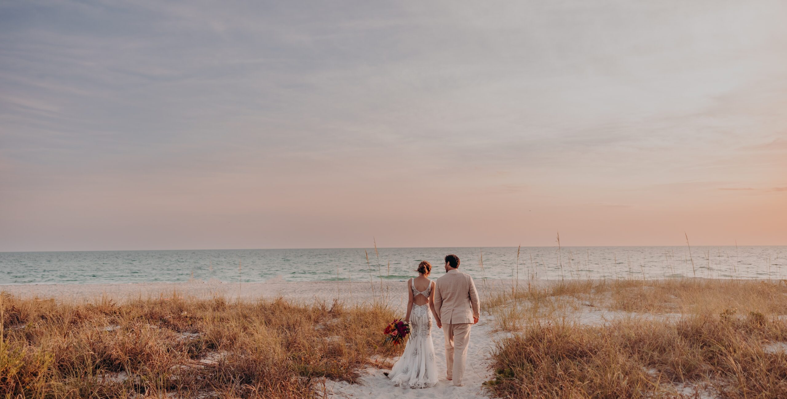 Bride and groom walking hand in hand at sunset on a Sarasota beach, captured by Angela Moon Photography.
