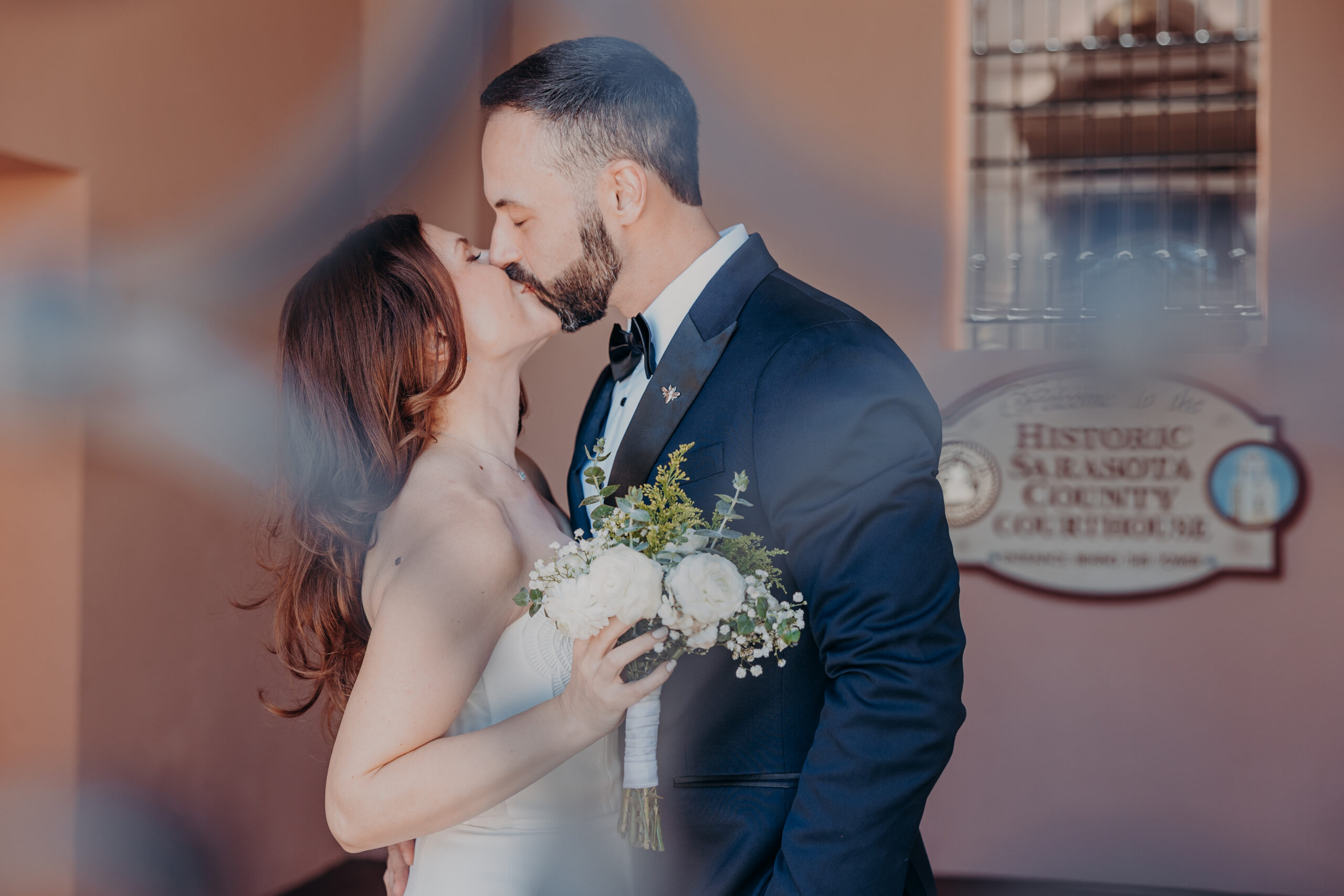 Diana and Robert kissing in front of the Historic Sarasota County Courthouse sign during outdoor wedding portraits in Sarasota FL