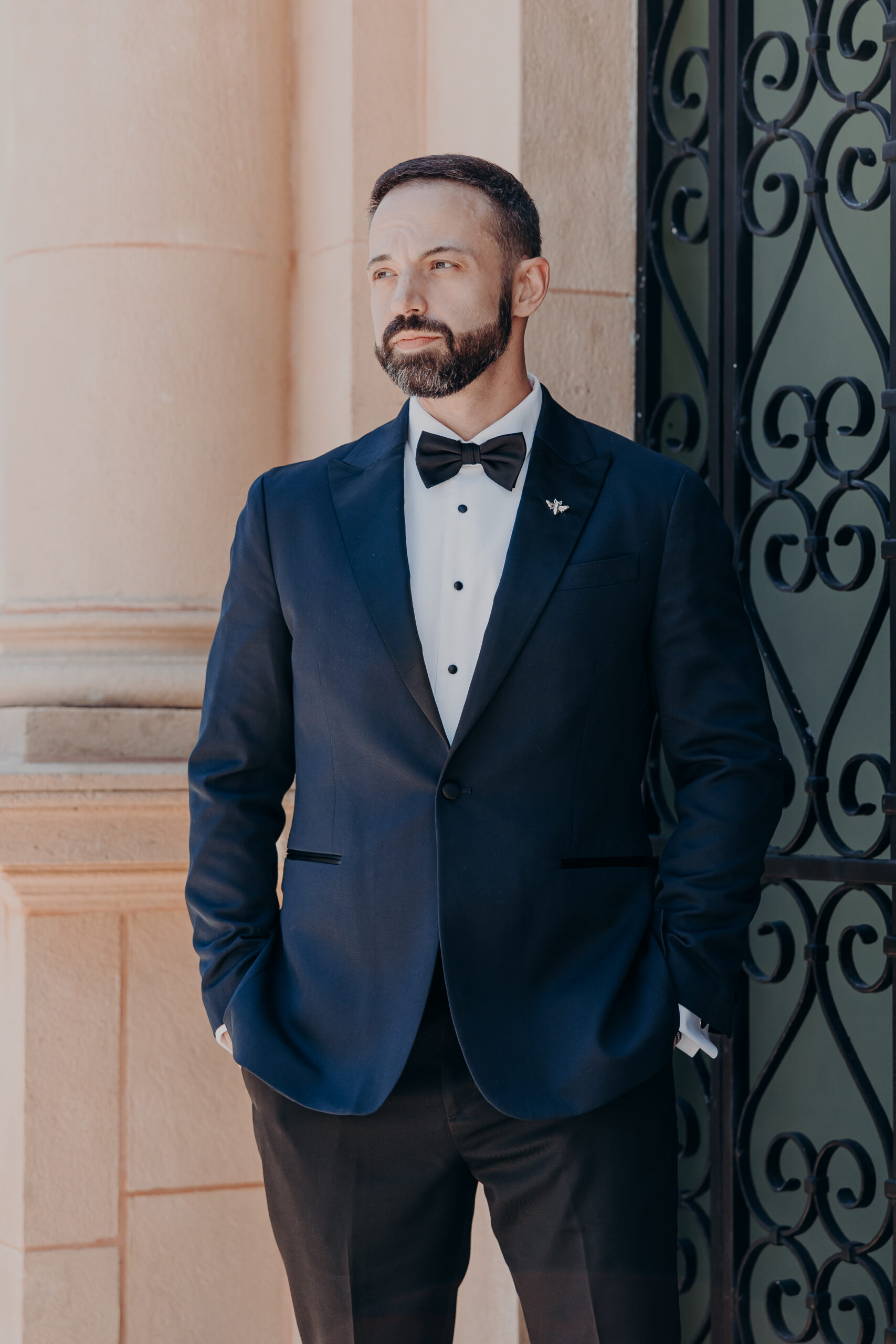 Groom Robert in a tuxedo looking off to the side beside the iron gates of the Historic Sarasota County Courthouse