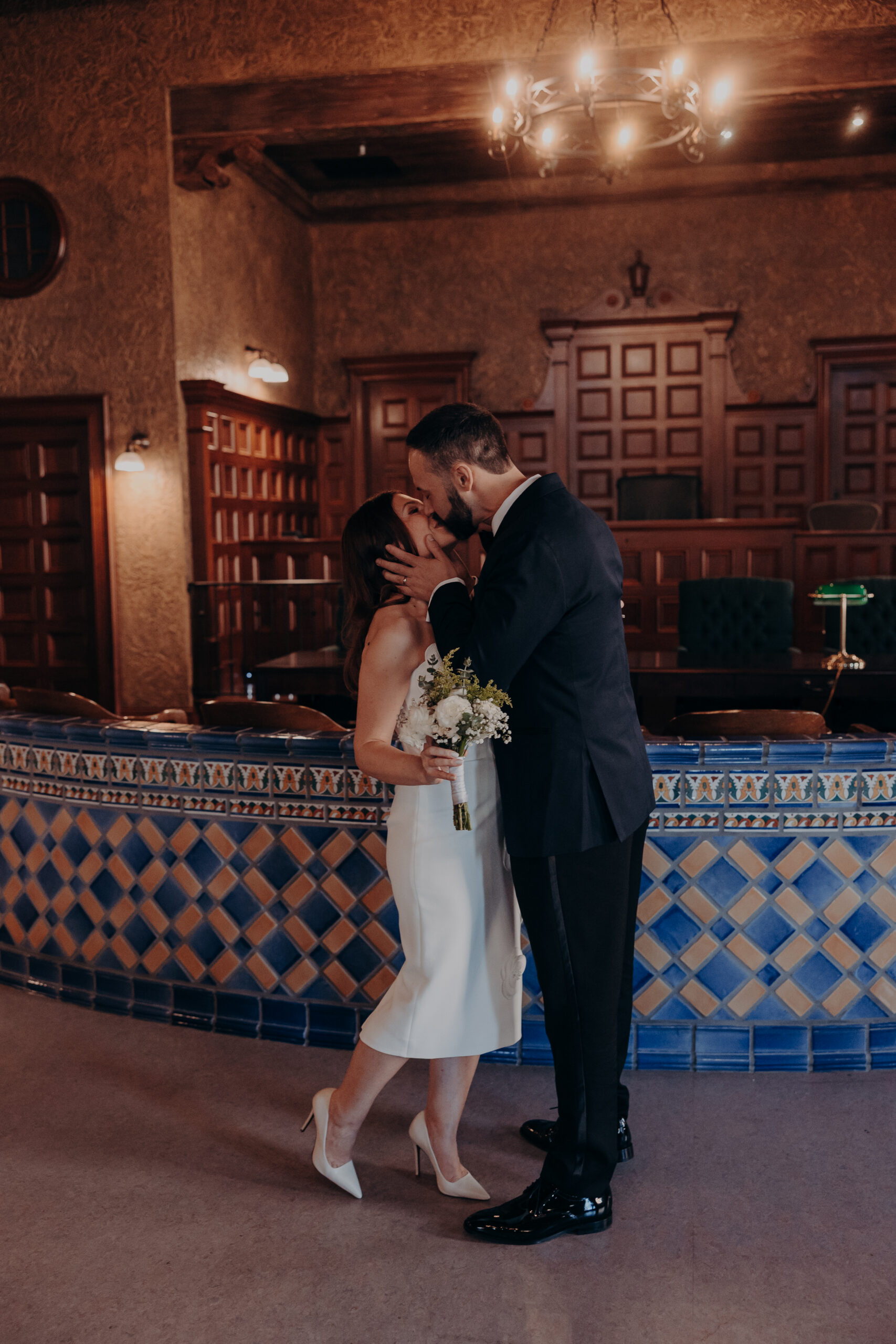 Couple sharing first kiss inside the Historic Sarasota County Courthouse with a glowing chandelier overhead