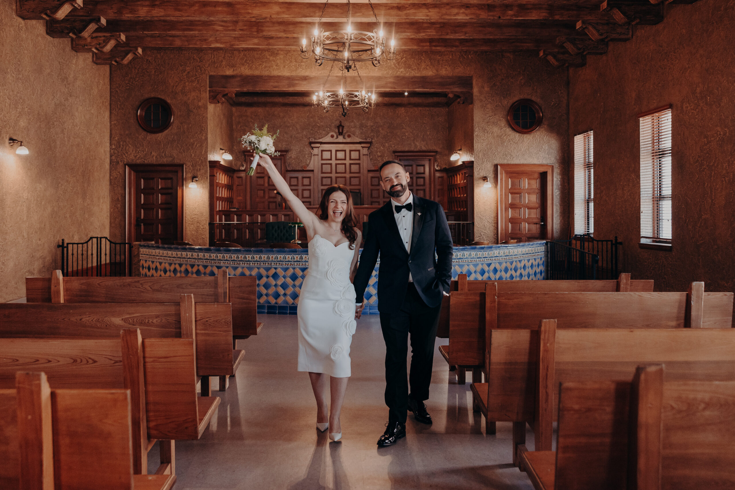 Bride raising bouquet in celebration as newlyweds walk up the aisle together at the Historic Sarasota County Courthouse