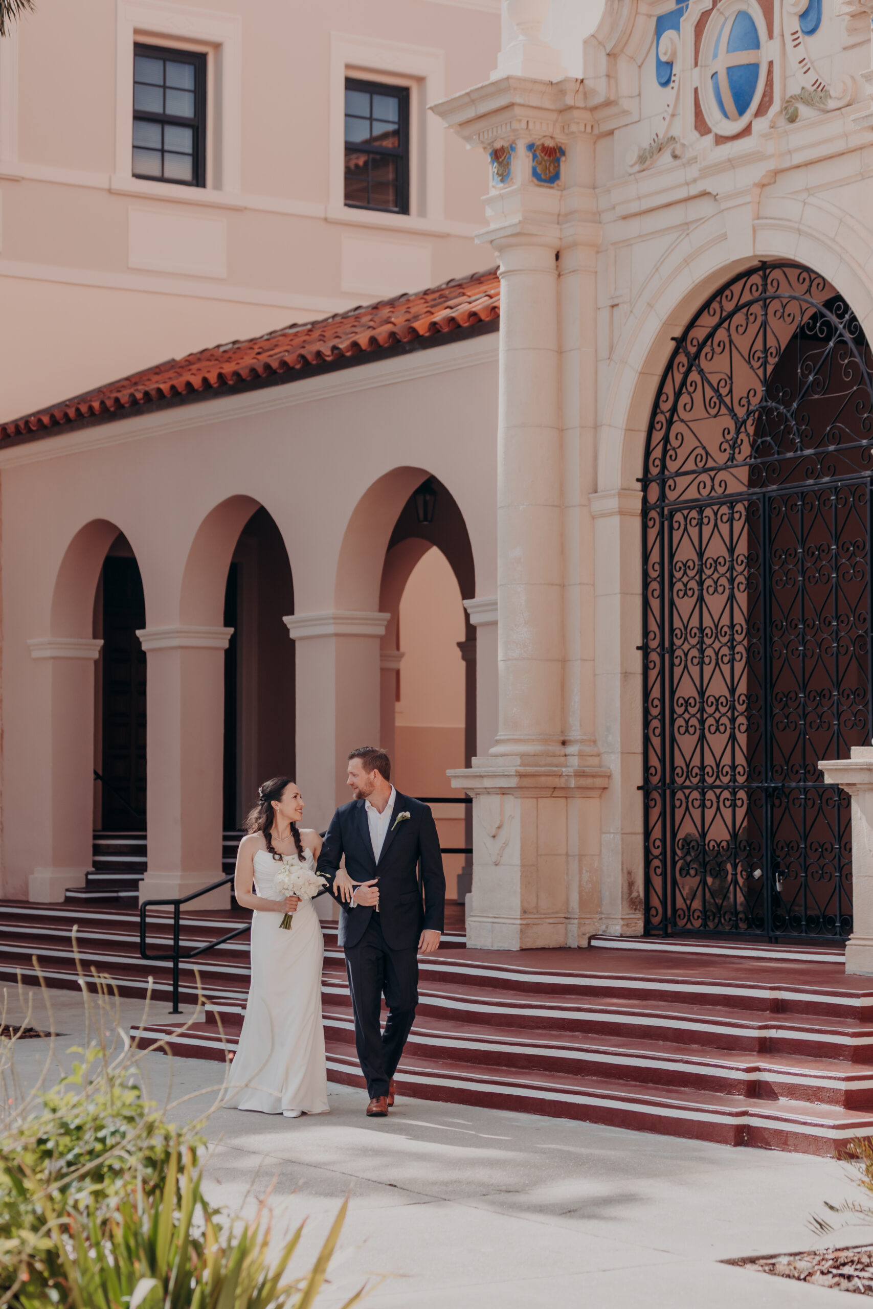 Liza smiling at Will during their Sarasota courthouse wedding ceremony with sunlight through the iron gates