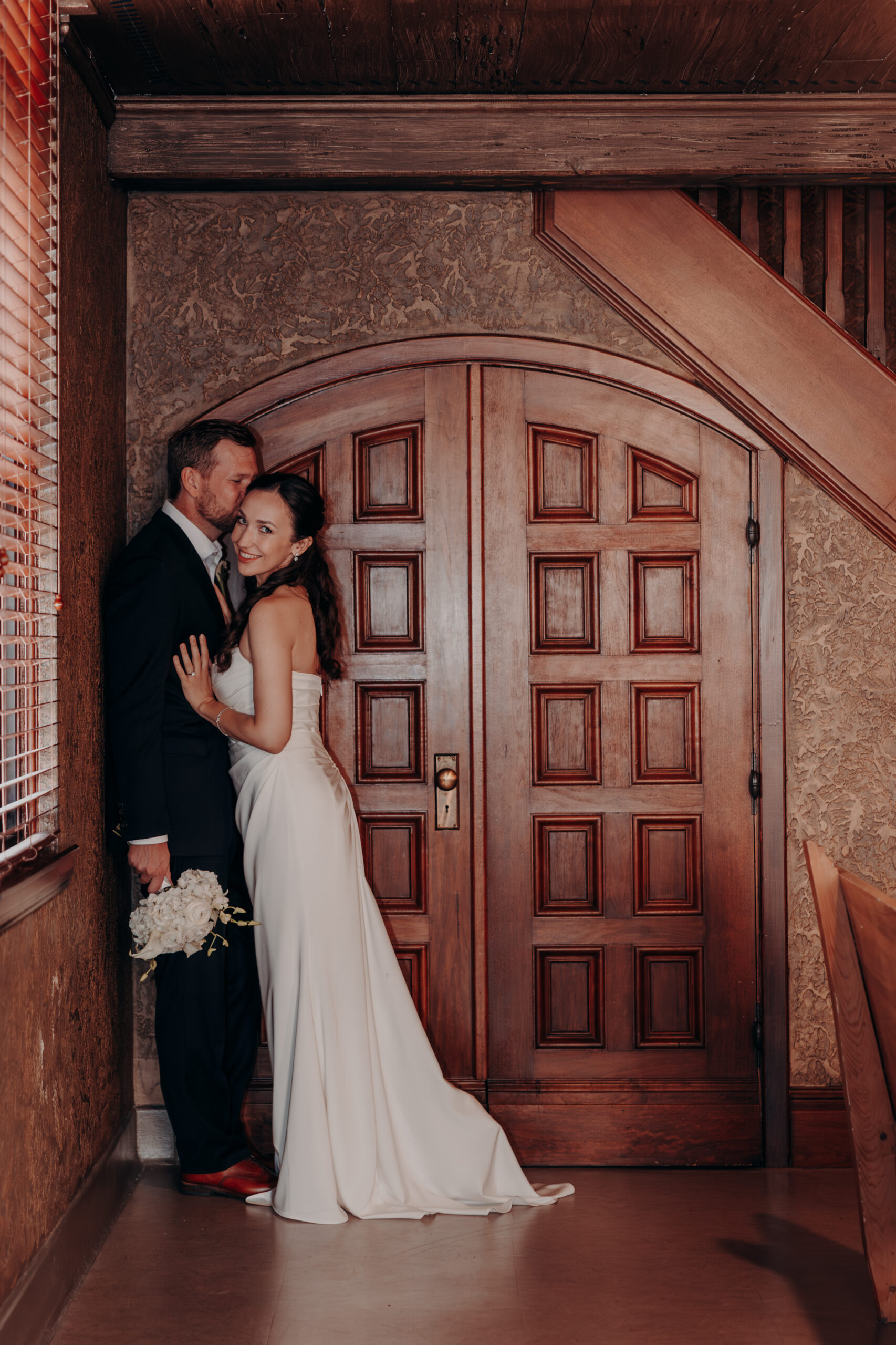 Liza and Will standing close together against the stone columns of the Sarasota Historic Courthouse