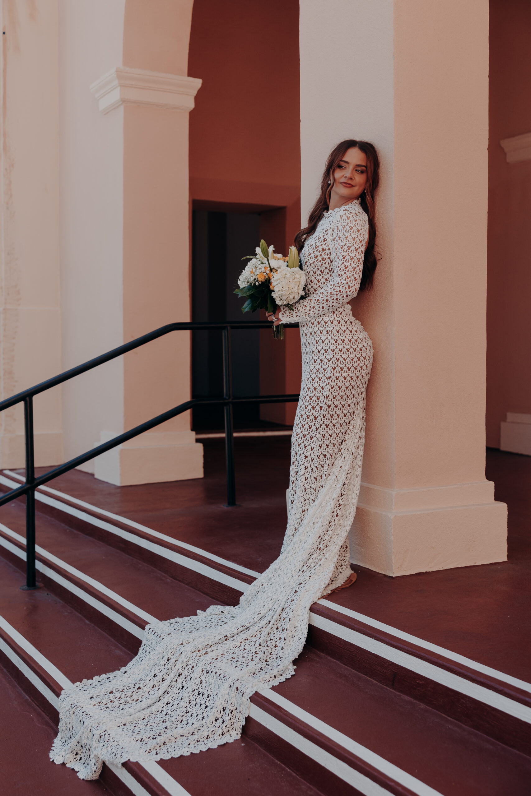 Mikaely holding her white bouquet on the exterior stairs of the Historic Sarasota County Courthouse in her lace wedding gown