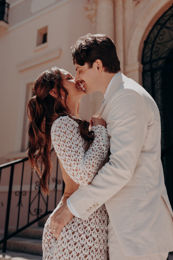 Mikaely and Chris laughing into a kiss outdoors in front of the ornate iron gate at the Historic Sarasota County Courthouse in Sarasota FL