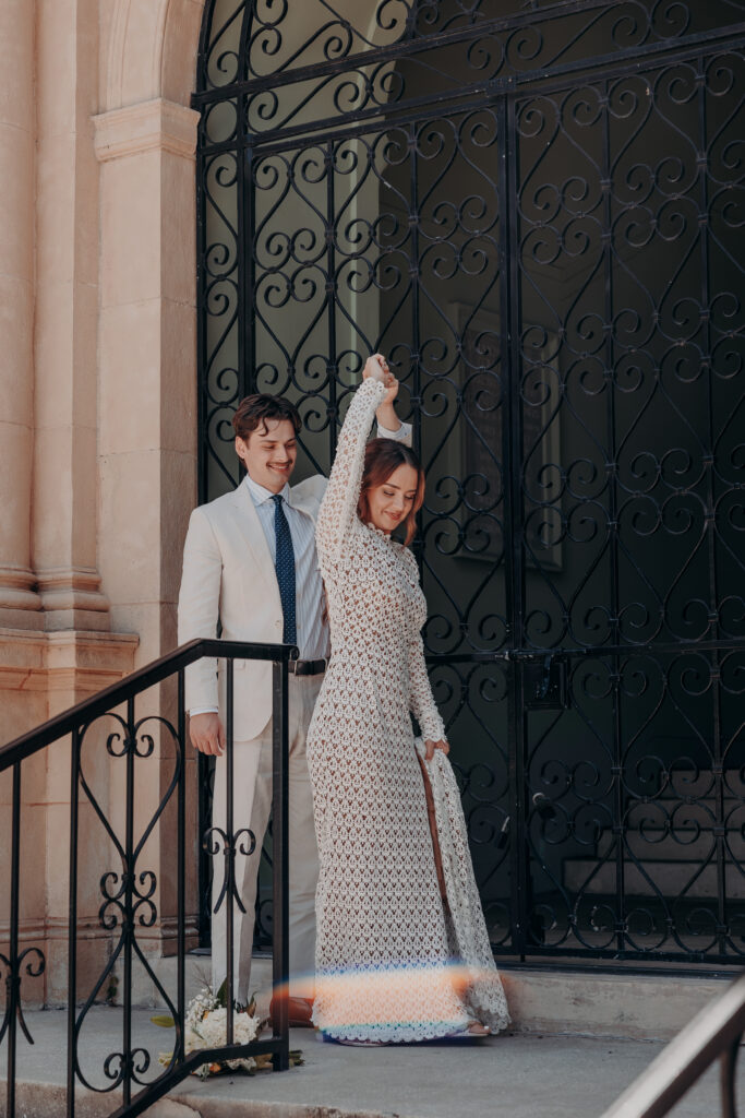 Mikaely twirling in her lace wedding gown while Chris watches at the iron gate of the Historic Sarasota County Courthouse Sarasota FL