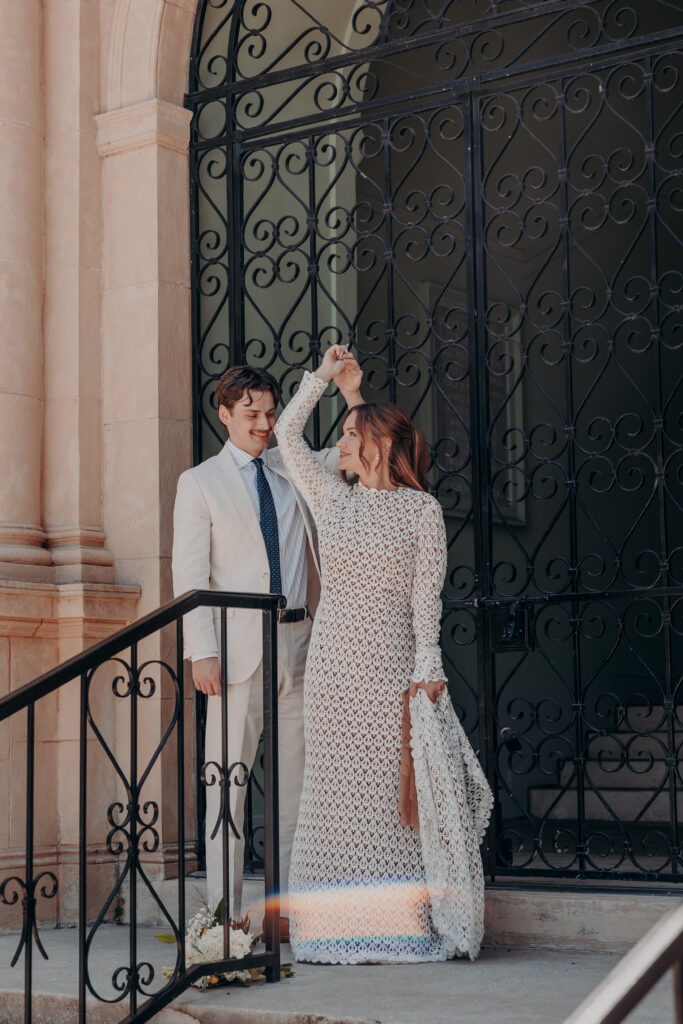 Chris holding Mikaelys hand as she twirls in her lace gown at the ornate iron gate of the Historic Sarasota County Courthouse Sarasota Florida