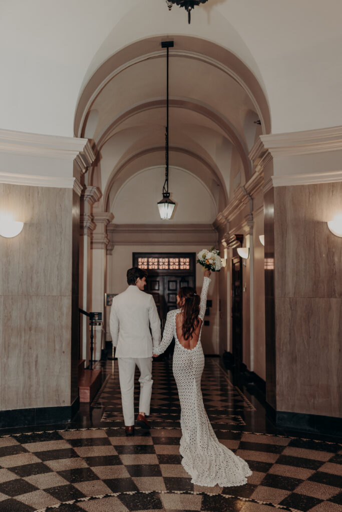 Mikaely and Chris walking hand in hand down the arched marble hallway inside the Historic Sarasota County Courthouse in Sarasota FL