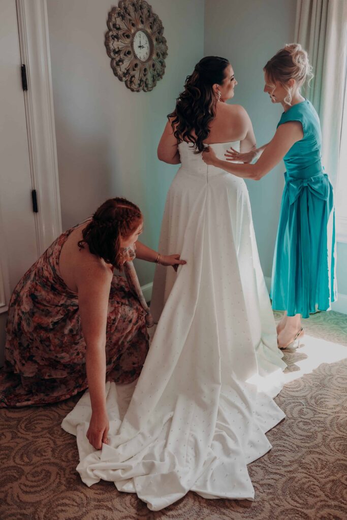 Bride being helped into her pearl-dotted wedding gown on wedding morning
