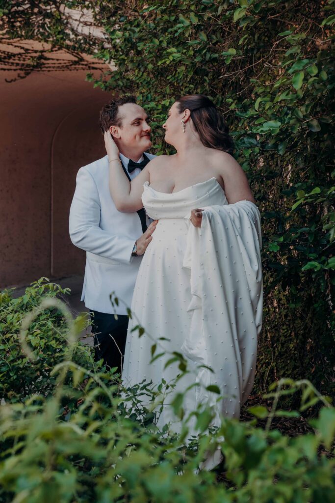 Bride cupping groom face both laughing in intimate portrait in ivy garden at Lakewood Ranch