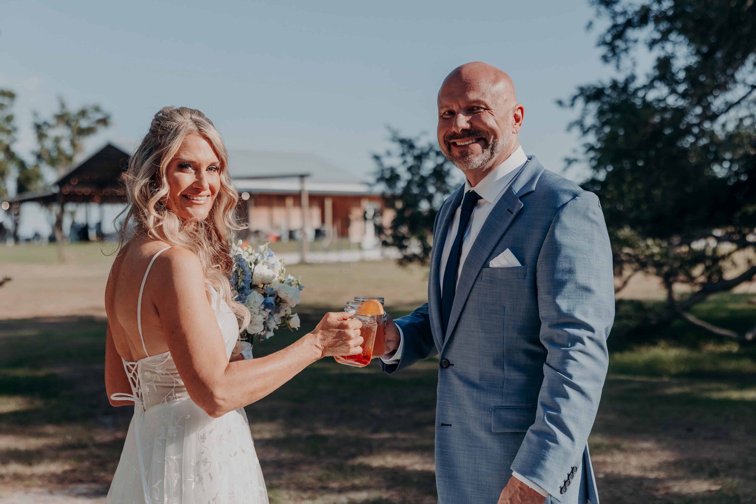 Bride and groom toasting mason jar drinks with pavilion in background at Brown's Grove Farm wedding