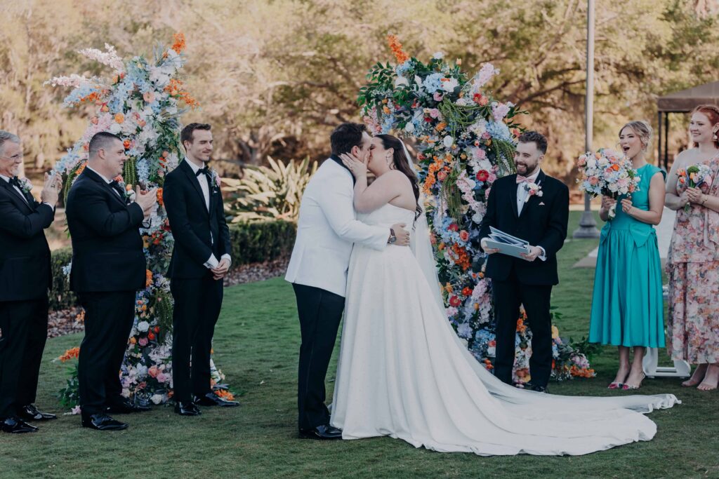 First kiss at Lakewood Ranch Golf and Country Club wedding with wedding party cheering and full floral arch