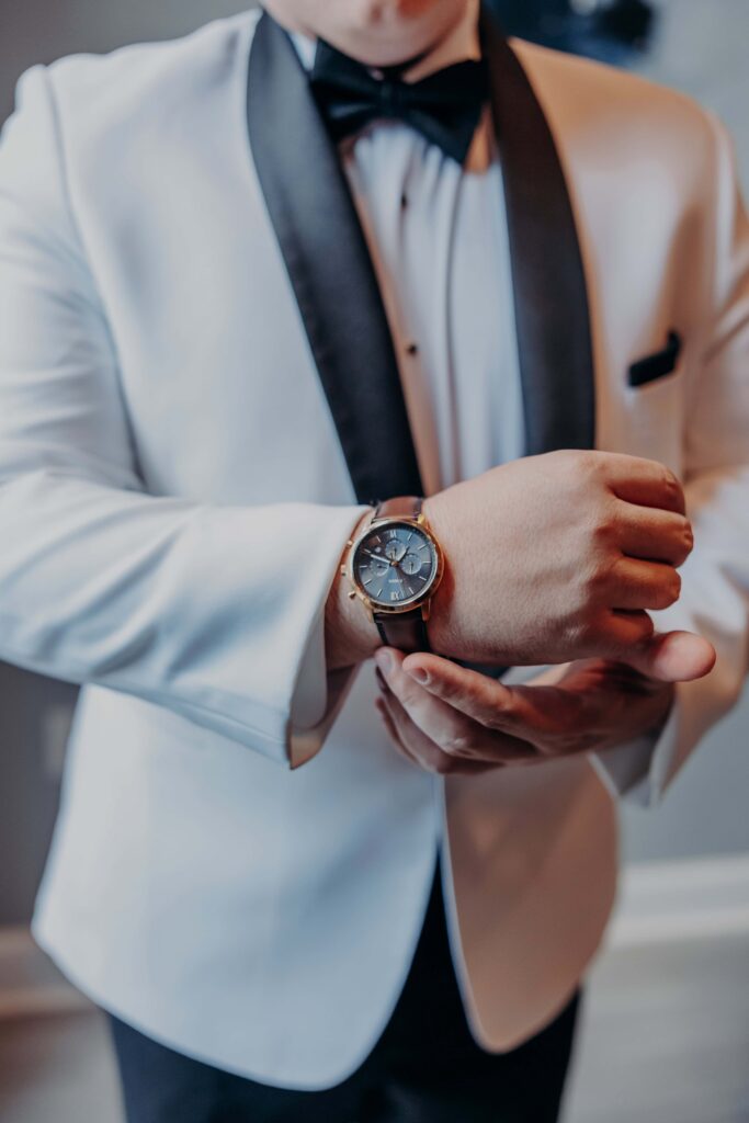 Groom detail white tuxedo jacket with black satin lapels fastening his watch