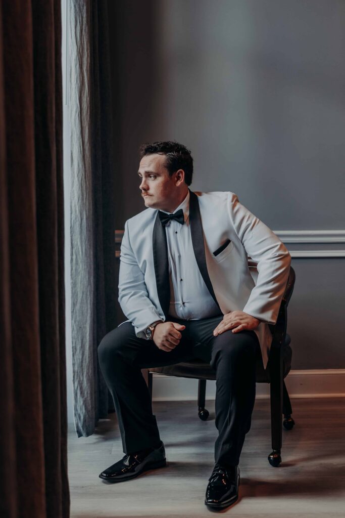 Groom in white tuxedo jacket seated by window at Lakewood Ranch Golf and Country Club