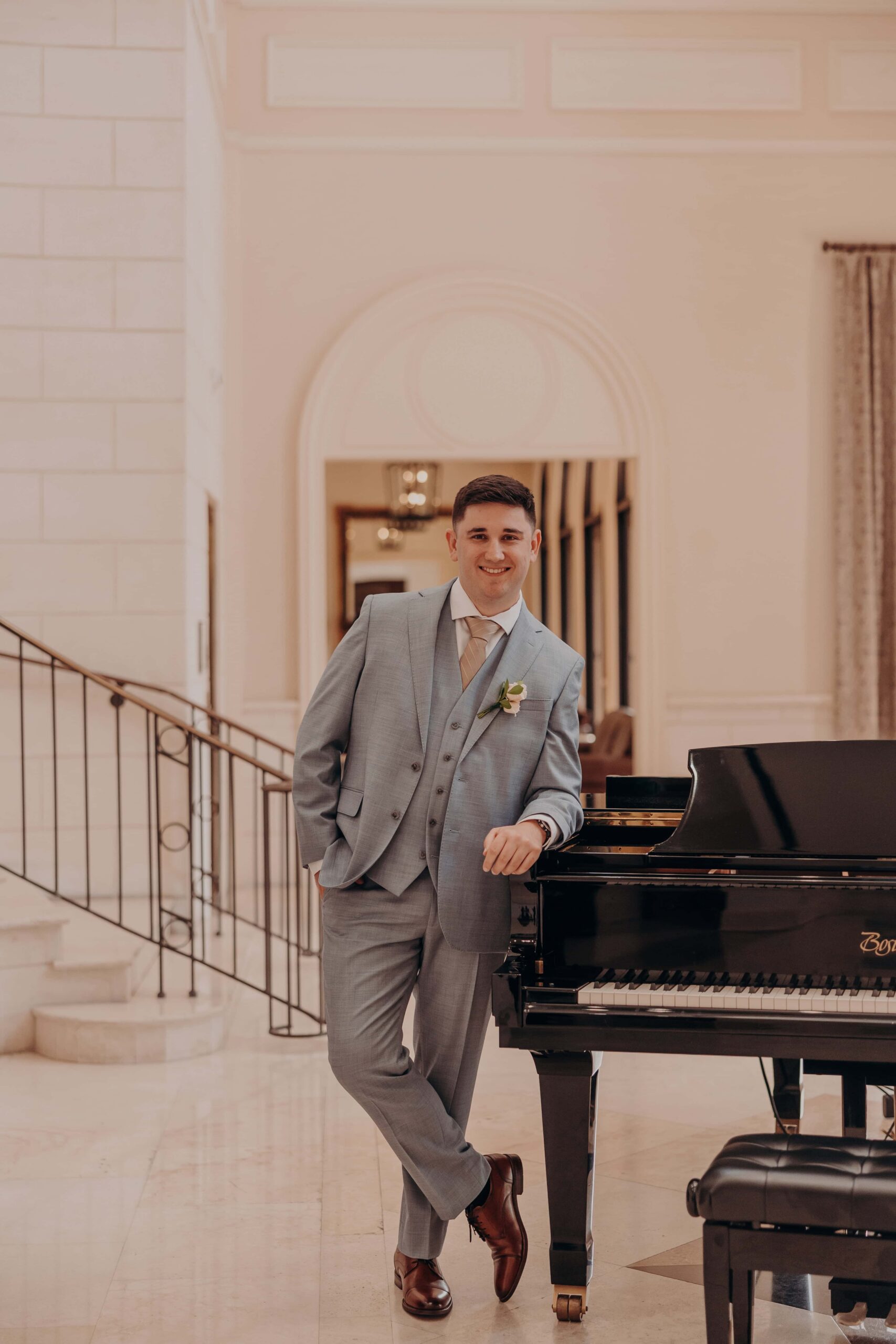 Groom Ryan sitting at the grand piano tying his shoes at Lakewood Ranch Golf and Country Club on his wedding morning