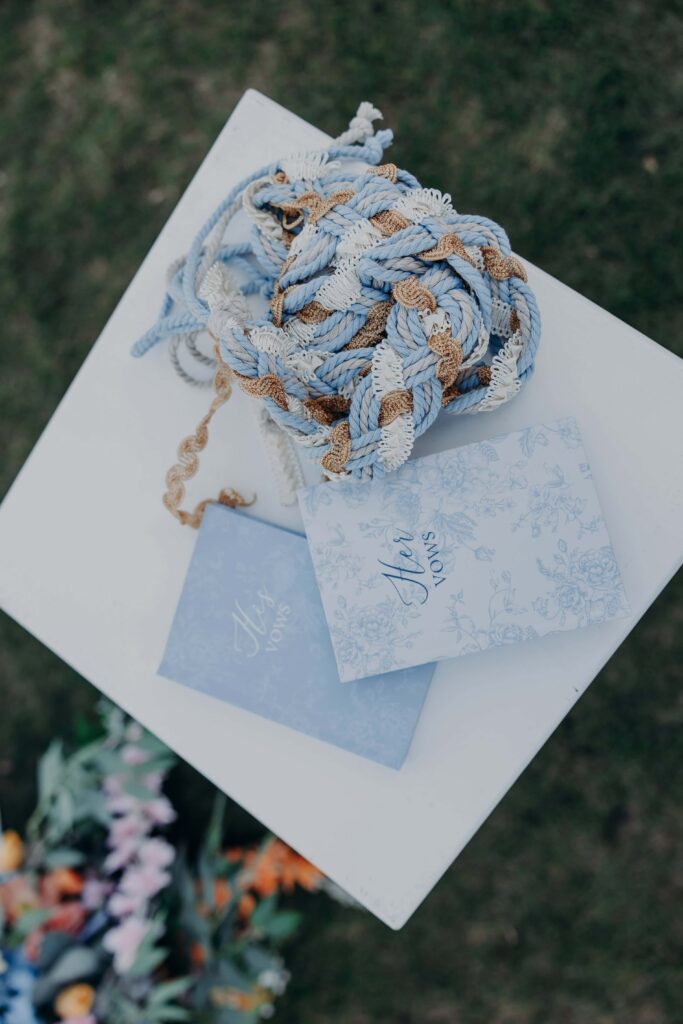 Handfasting ceremony cords coiled on pedestal beside His Vows and Her Vows books at outdoor ceremony