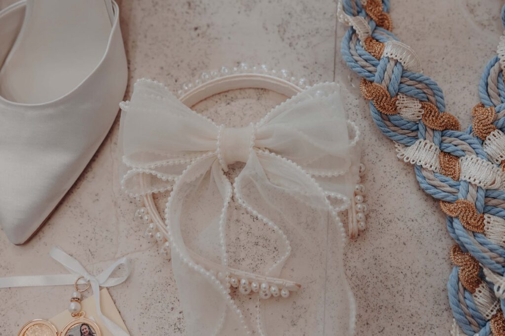 Wedding details flatlay with pearl bow hairpiece something blue braided cord and heels