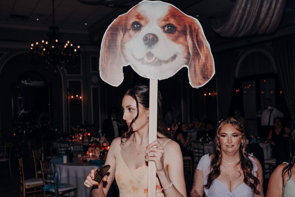 Wedding guest holding giant Cavalier King Charles Spaniel dog face cutout on dance floor at reception