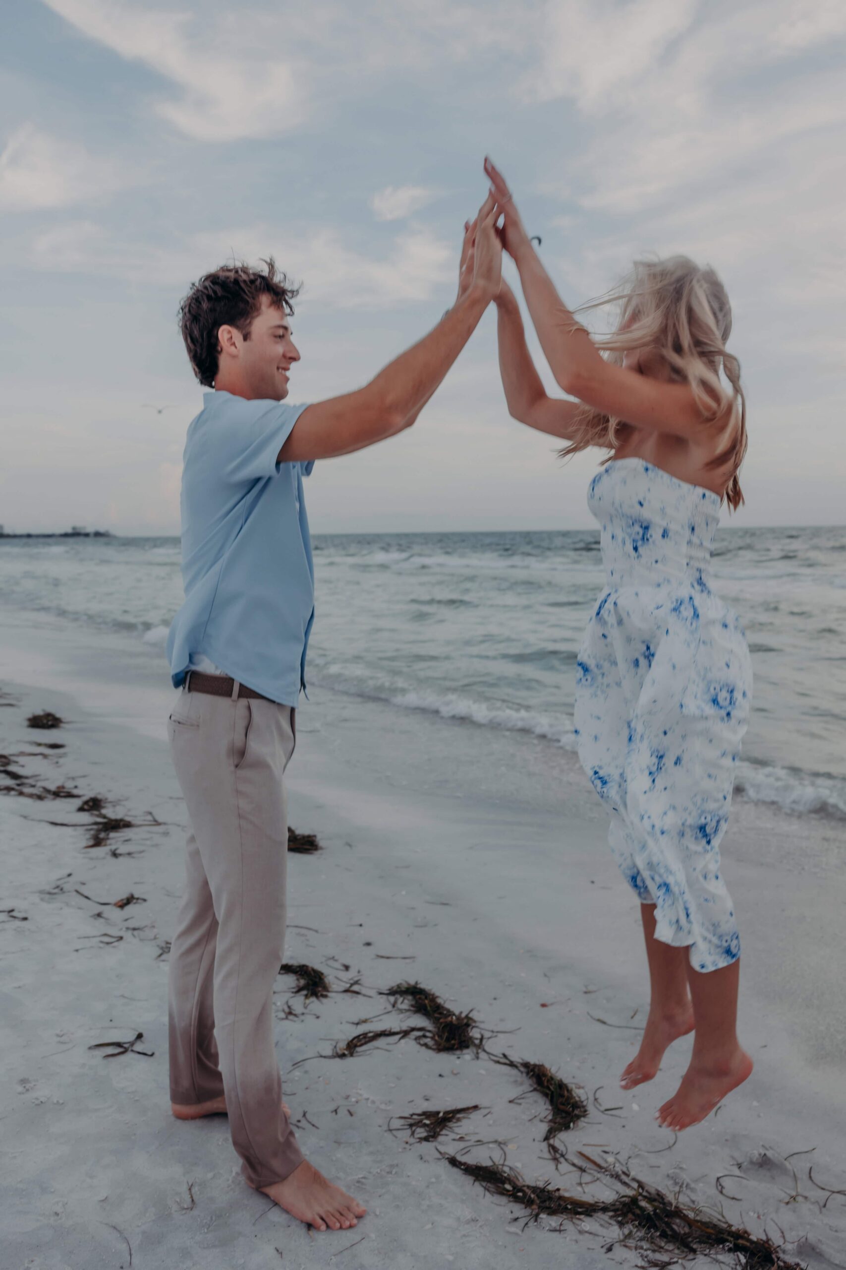 Playful jumping high five during Lido Beach engagement photos in Sarasota