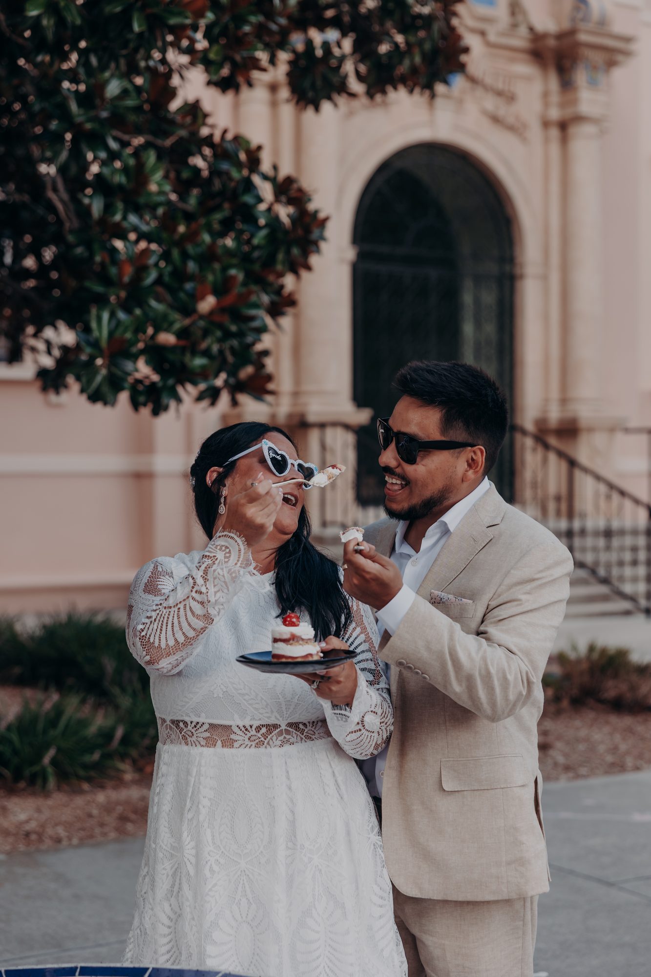Karlee in heart-shaped sunglasses feeding Caleb a bite of their Whole Foods wedding cake