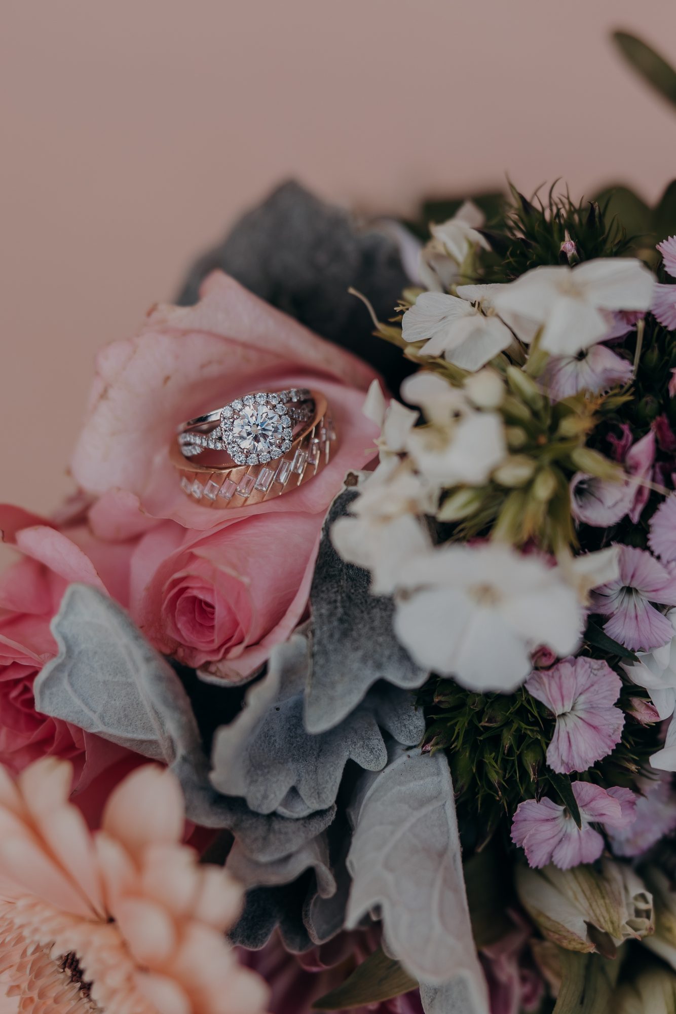 Karlee and Caleb's wedding rings resting on a pink rose in their bouquet