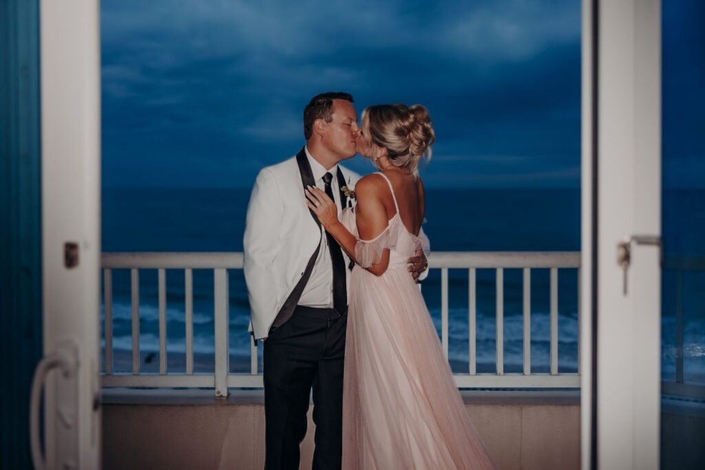 Bride and groom kissing on an oceanfront balcony at dusk during their Lido Beach Resort wedding in Sarasota, FL